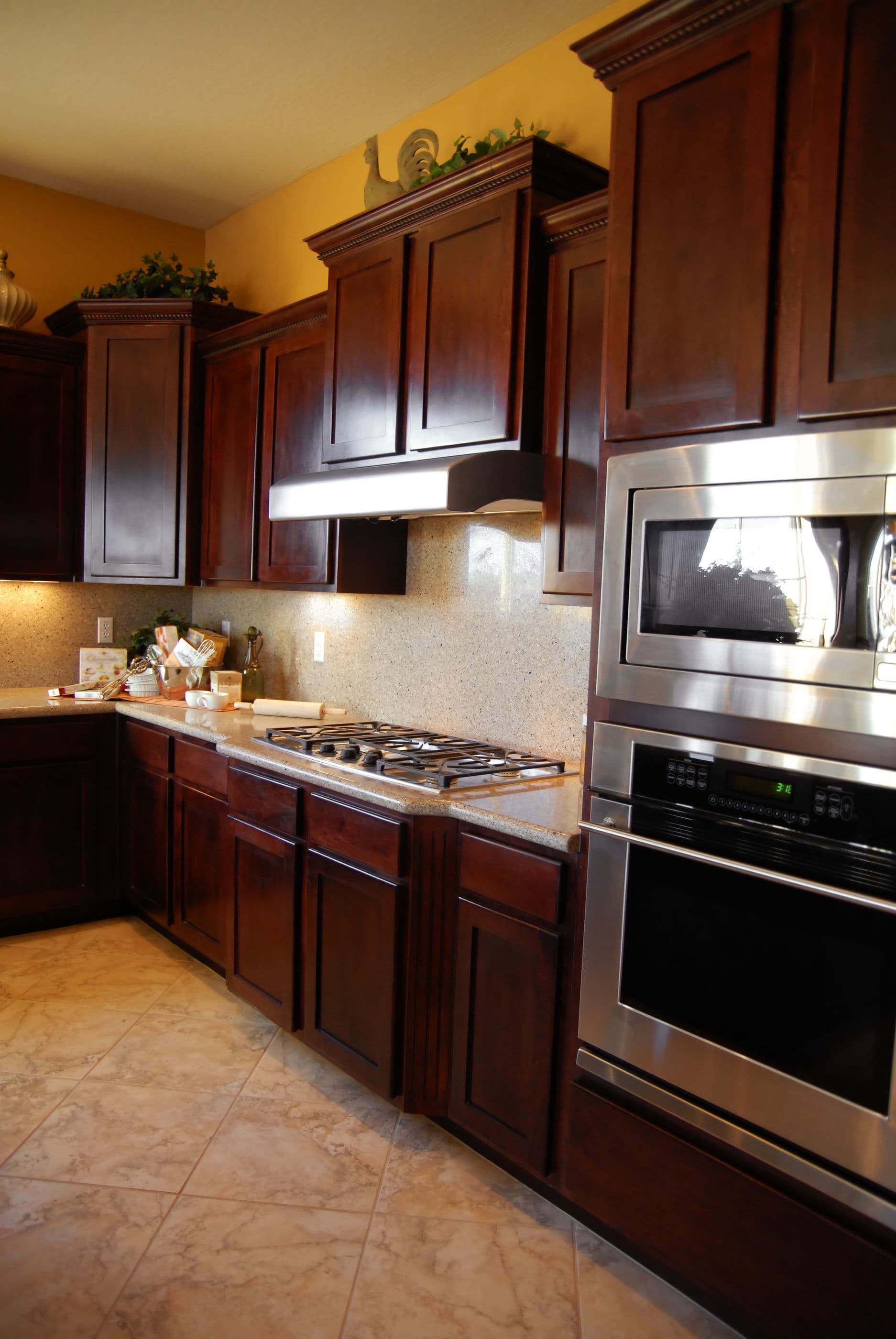 Kitchen with dark cherry wood cabinets, gas cooktop, stainless steel built-in microwave and oven, granite countertop, and yellow accent walls